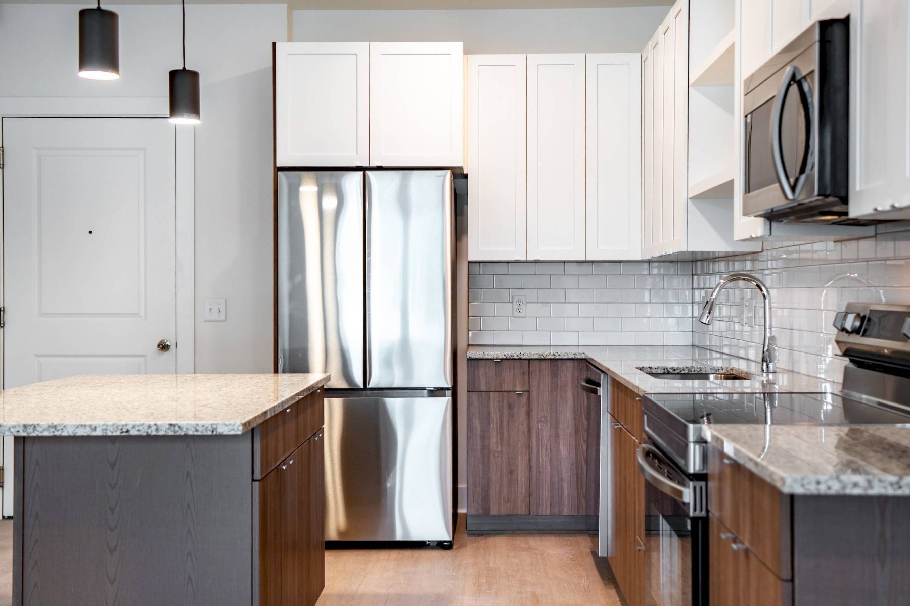 Modern kitchen with stainless steel appliances, white cabinets, subway tile backsplash, and a granite island.
