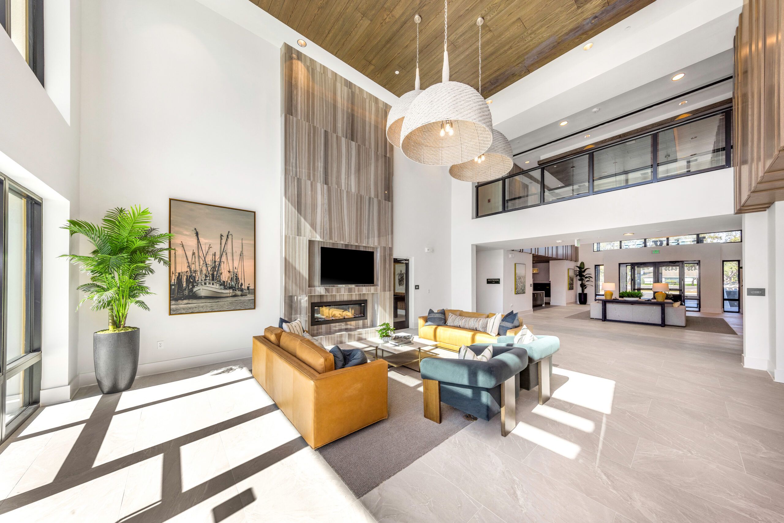 Modern, sunlit lounge with sofas, fireplace, large windows, high ceiling, and contemporary decor.