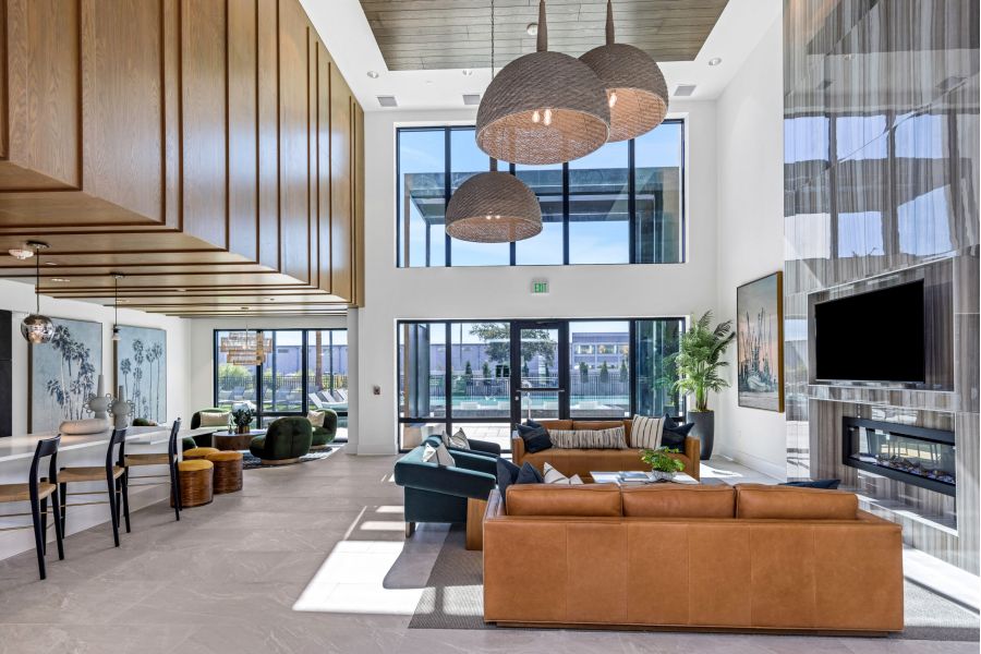 Modern, spacious lounge with large windows, tan sofas, hanging lights, and a wall-mounted TV.