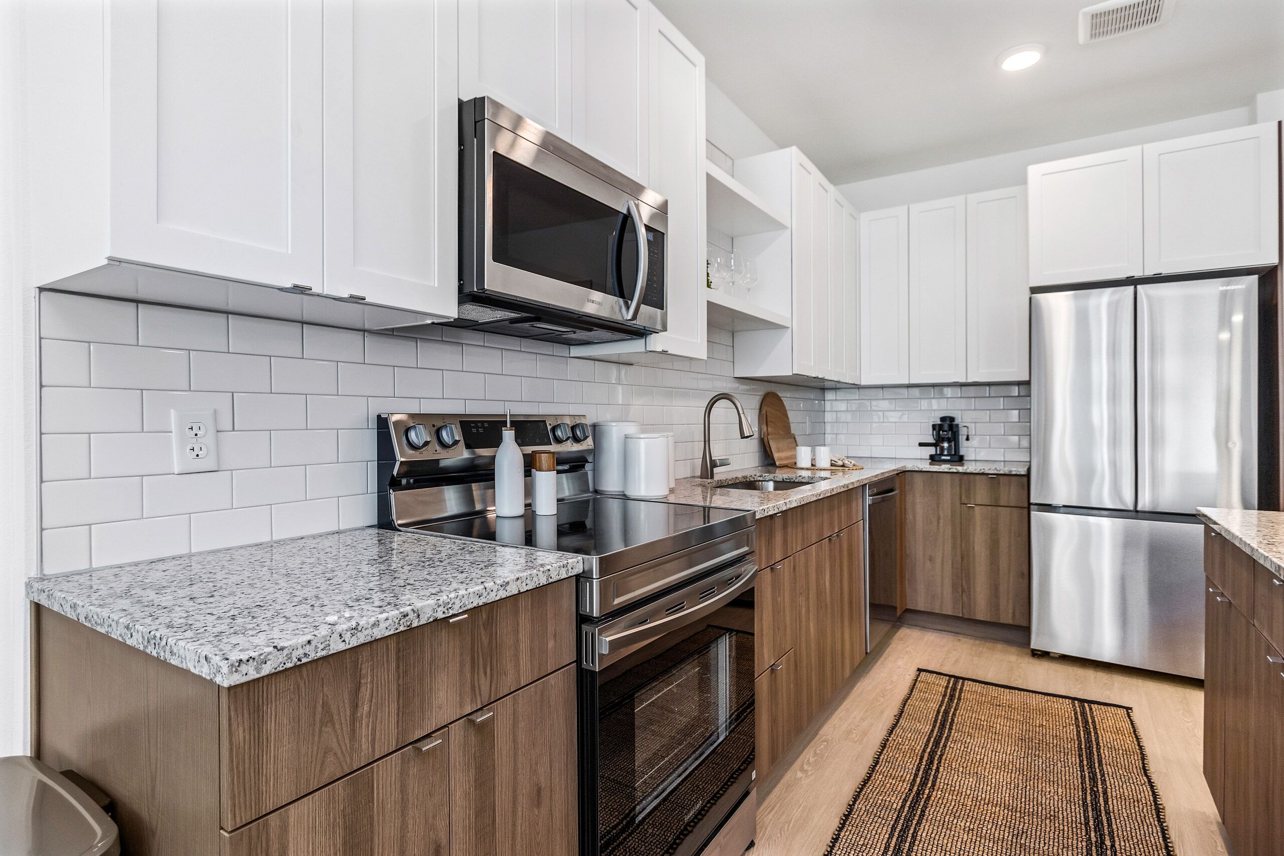 Modern kitchen with white cabinets, stainless steel appliances, granite countertops, and a woven rug.