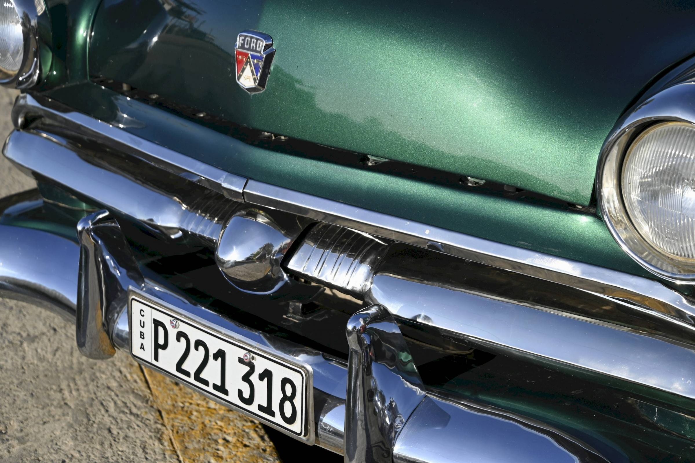 Close-up of a green vintage Ford car's front grill, bumper, and Cuban license plate P221318.