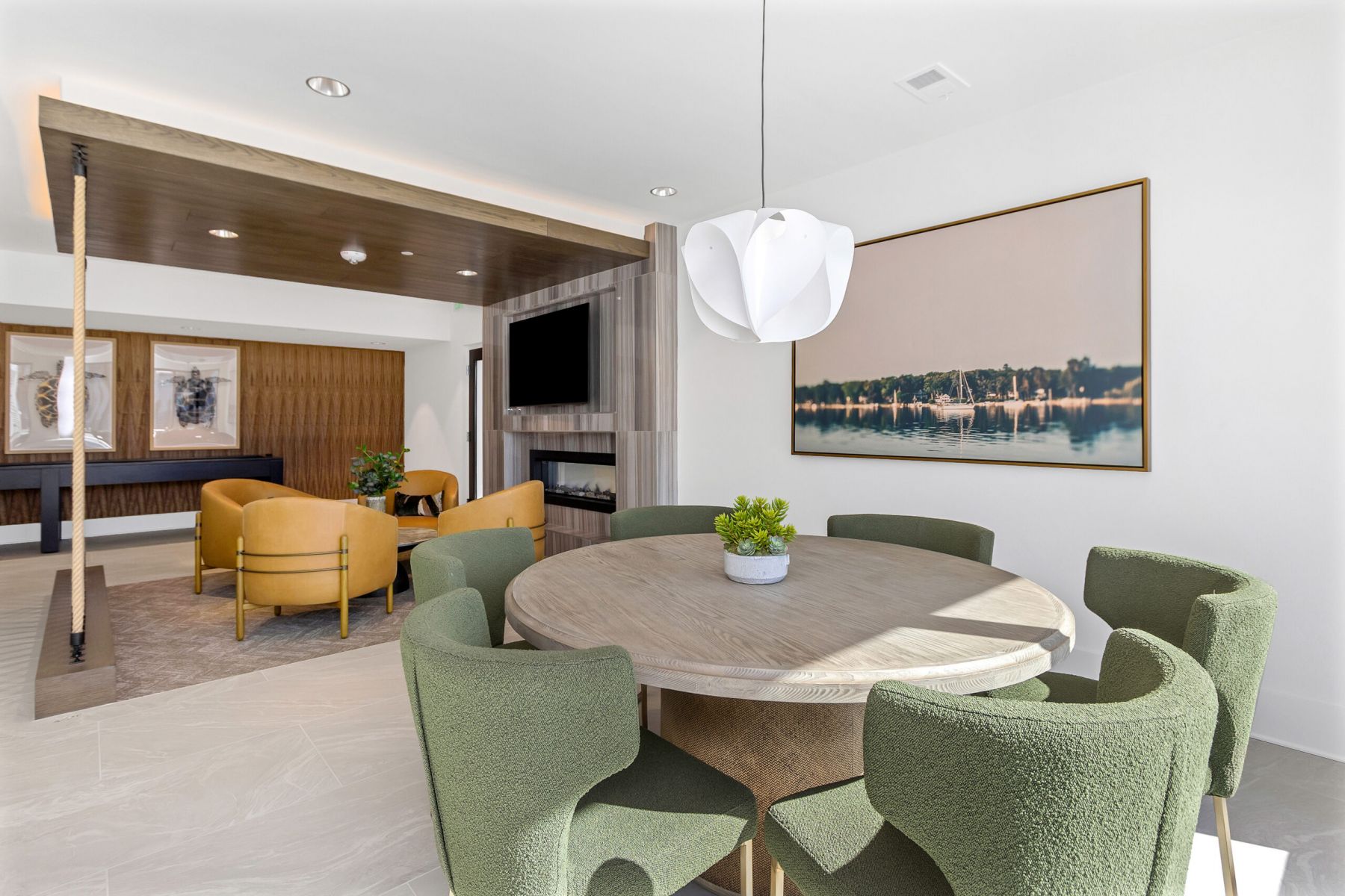 Modern dining area with a round table, green chairs, and a living space with yellow armchairs in the background.